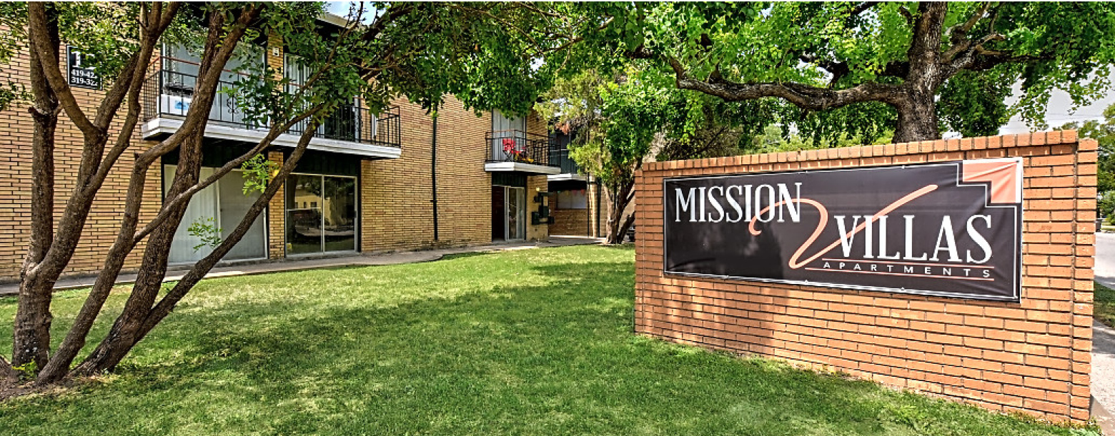 Exterior view of Mission Villas apartments in San Antonio, TX. Signage is displayed on the right with the a building to the left.