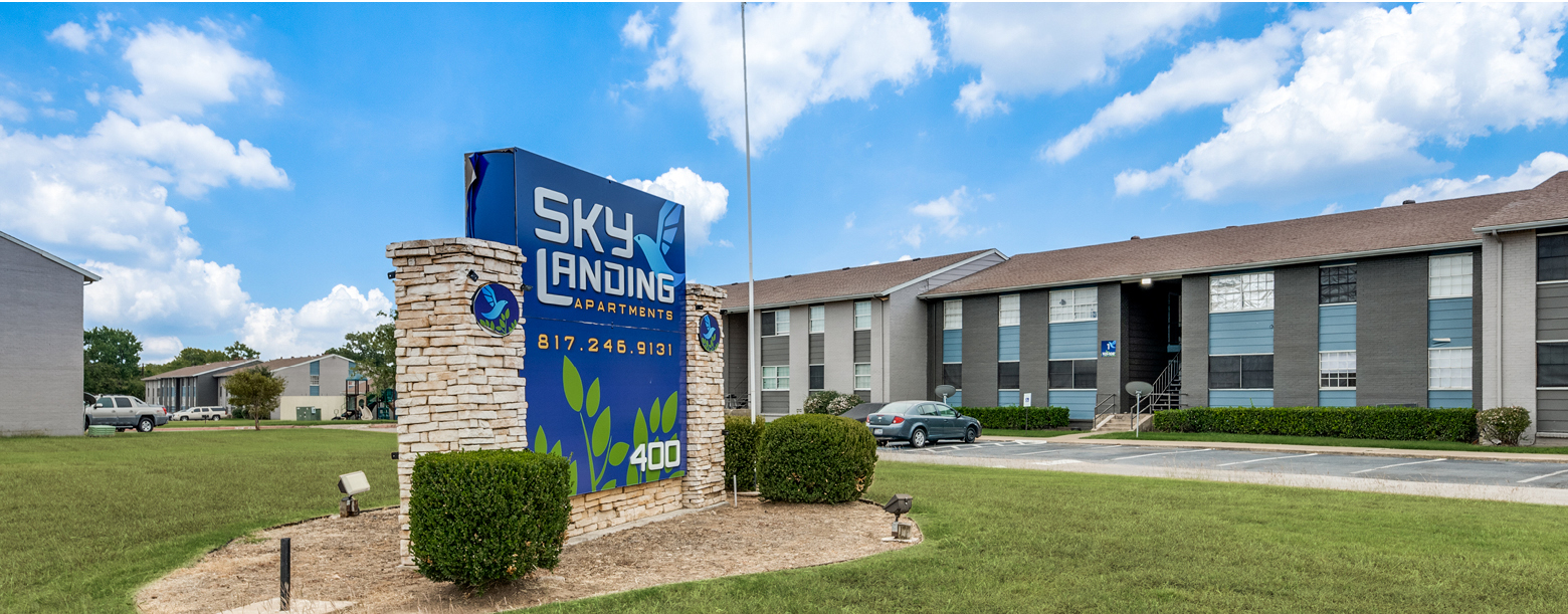 Exterior view of Sky Landing apartments in White Settlement, TX featuring apartment buildings and signage.