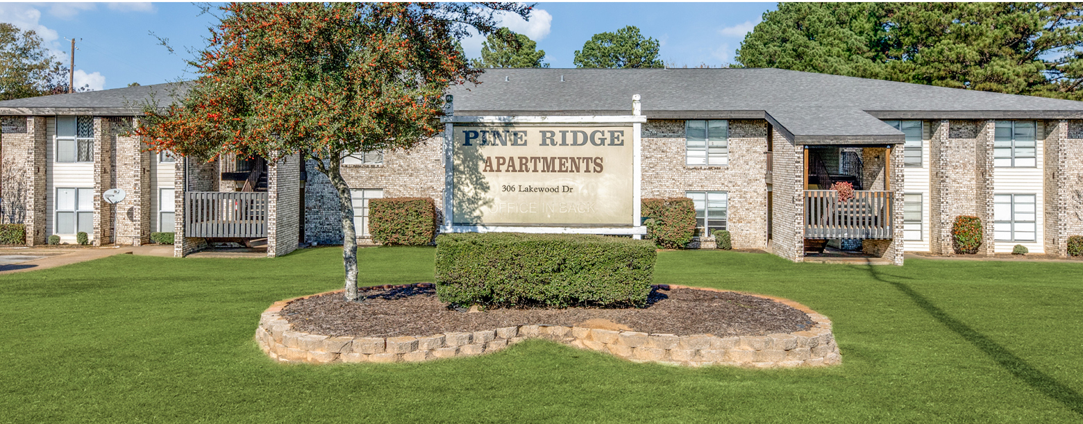 The Pine Ridge signage sits at the center of the image with a clear view of the apartment building in the background.
