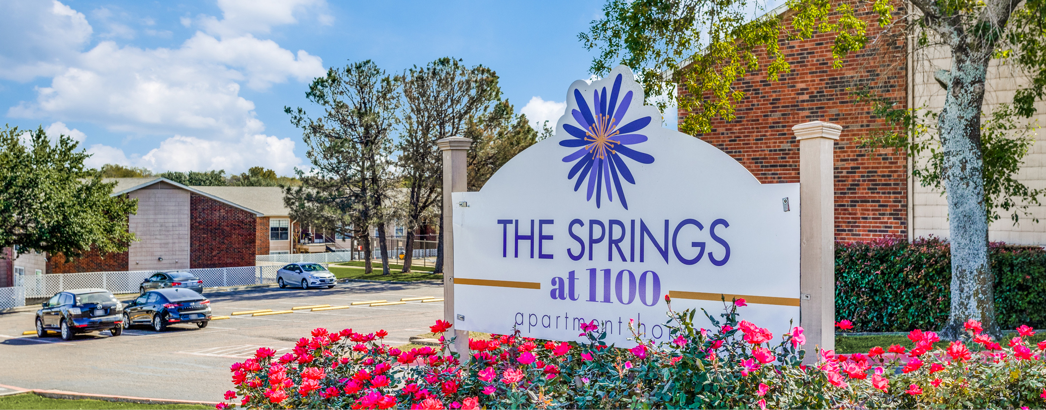 A view of the signage at The Springs at 1100, along with several buildings and a parking lot in the back.