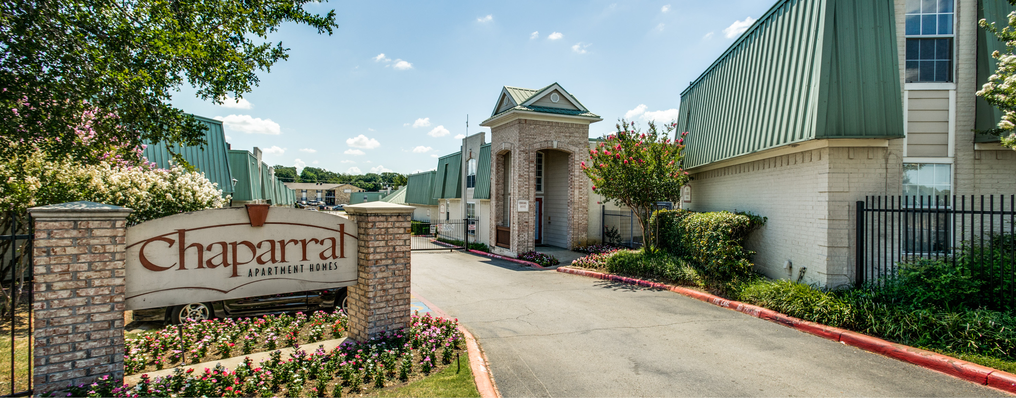 The entrance to Chaparral Apartment Homes with the signage to the left and buildings in the background and the right.